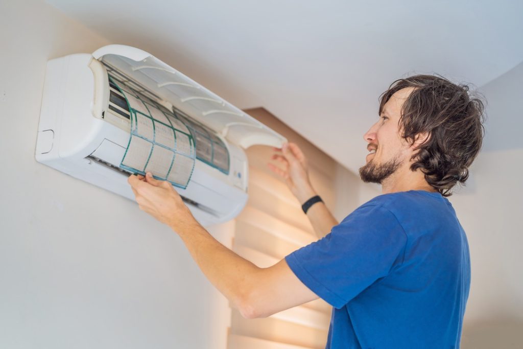 Homeowner performing routine maintenance on ductless mini-split AC by changing filter